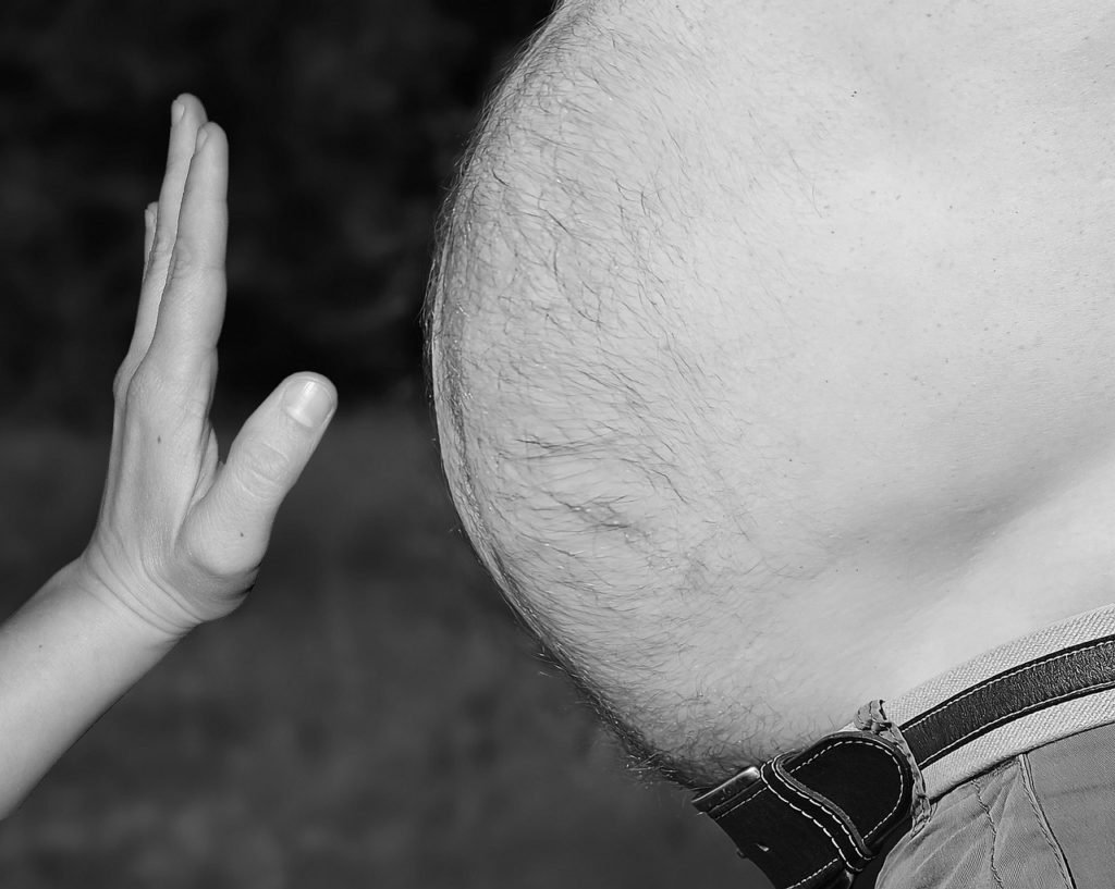 Photo of a hand in front of an obese belly.